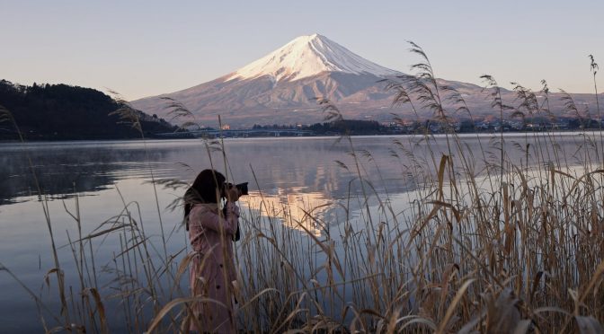 woman taking picture near lake with view of mount fuji