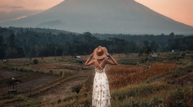 back view of a woman wearing white dress and sun hat standing on the farmland