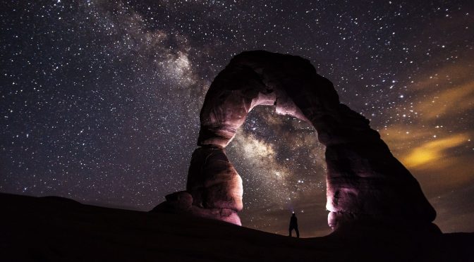 person standing under a rock formation on a starry night